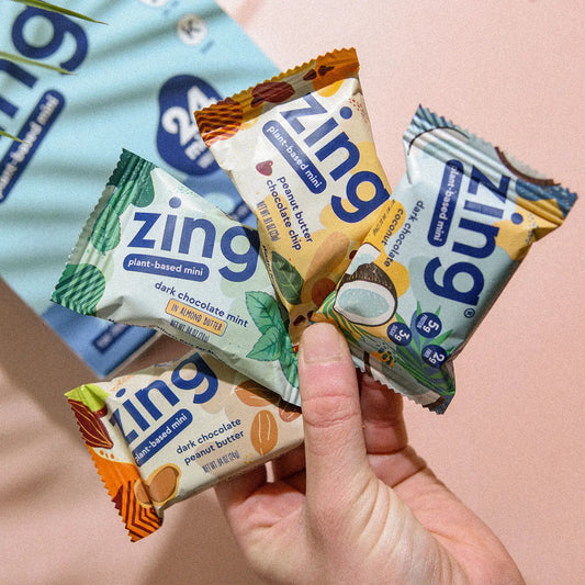 someone holding the four flavors of zing bar minis: dark chocolate coconut, peanut butter chocolate chip, dark chocolate mint, and dark chocolate peanut butter
